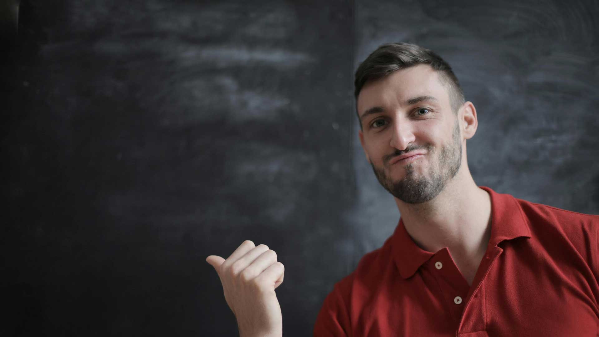 Lehrer zeigt stolz auf eine Schwarze Tafel